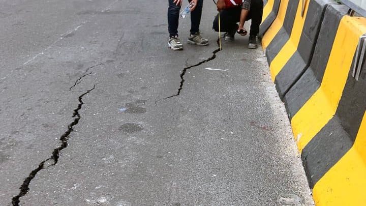 Cracks in a roadway with concrete barriers on right side