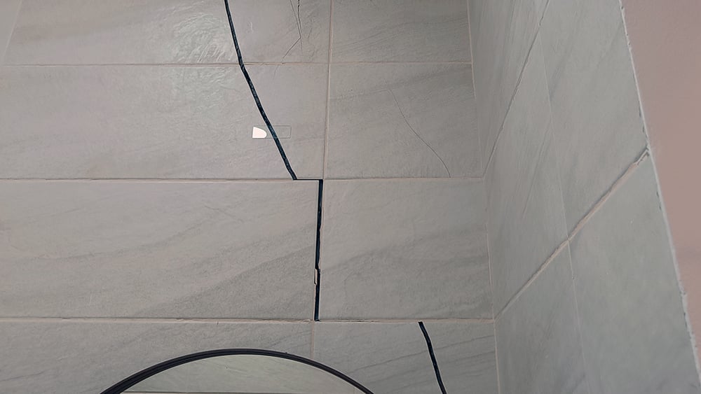 Ground settlement caused cracking marked on a tile wall in a villa. Crack measuring monitor attached to the wall.