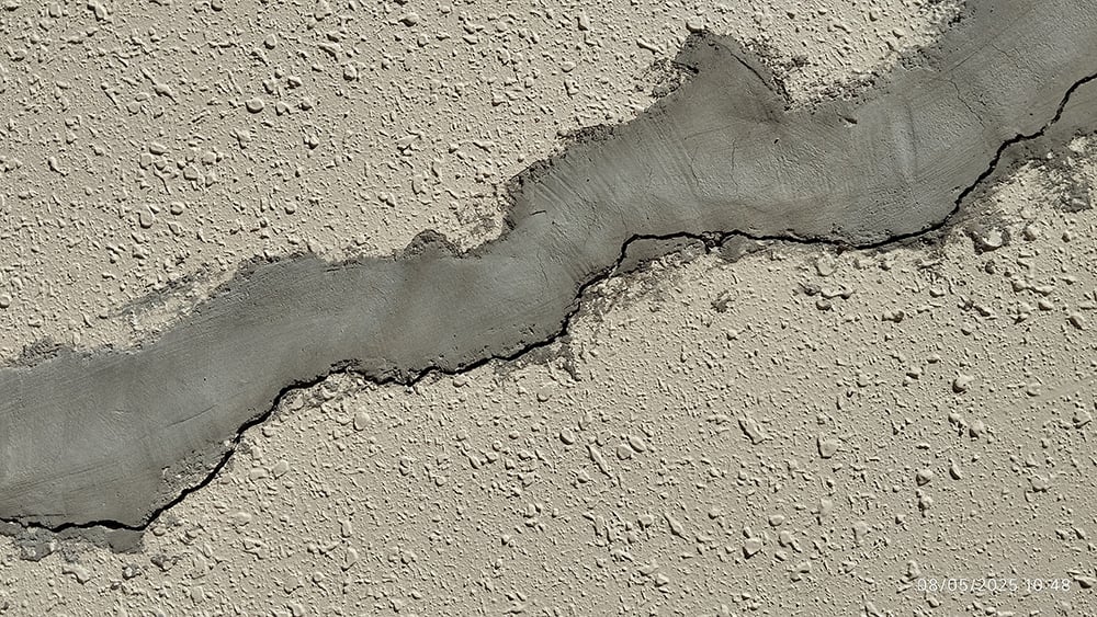 Closeup view of diagonal crack reappearing from previously patched external villa wall caused by ground settlement