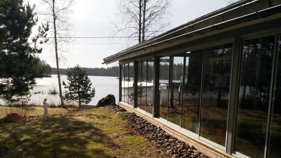 Kesämökin lasitettu terassi kuvattuna keväistä järvimaisemaa vasten.