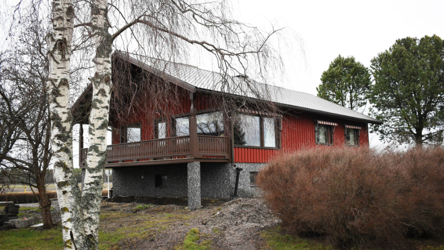 Kaksikerroksinen omakotitalo kuvattuna sateisena kesäpäivänä. Talon vierusta on kaivettu parvekkeen alta auki.