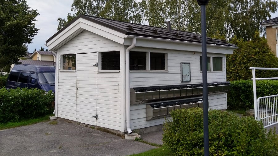 Taloyhtiön pieni varastorakennus, jonka kylkeen on kiinnitetty metallisia postilaatikkoja.