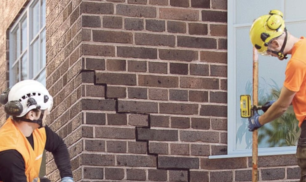 Two technicians monitor a laser receiver during a geopolymer injection sequence.