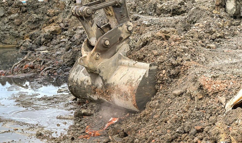 Grävskopa gräver i sand och lera på byggarbetsplats.