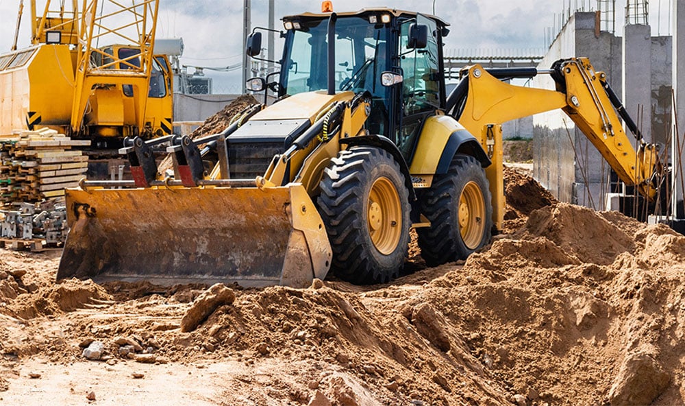 En grävmaskin i arbete med sand som underlag på en byggarbetsplats.