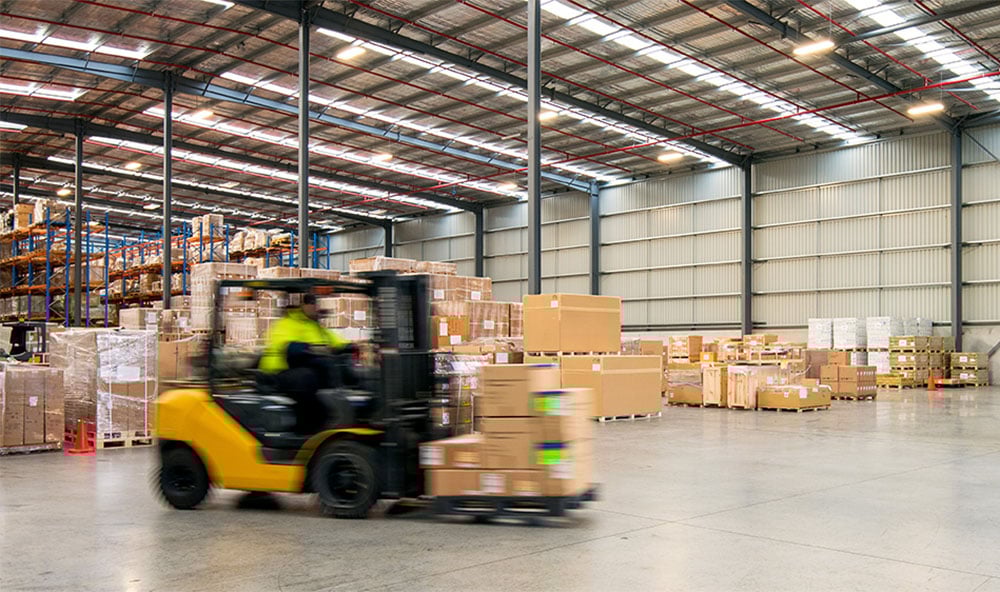 En truck kör i farten med bruna lådor på gaffeln i ett logistikcenter