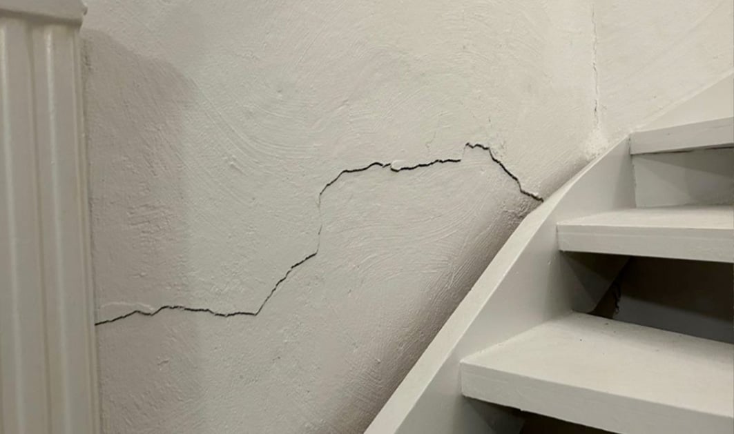 Närbild på vit innervägg i villa som är drabbad av väggsprickor / sättningssprickor, med närliggande trappa