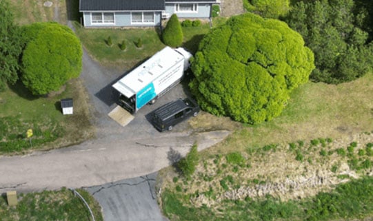 Drönarbild över en villatomt på landsbygden med stor grön tomt, och Geobears lastbil parkerad framför huset.