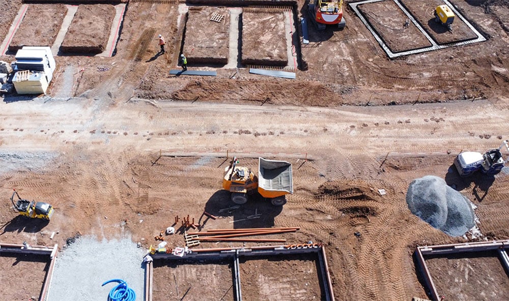 Drönarbild på en byggarbetsplats med jord, grus och olika slags maskiner.