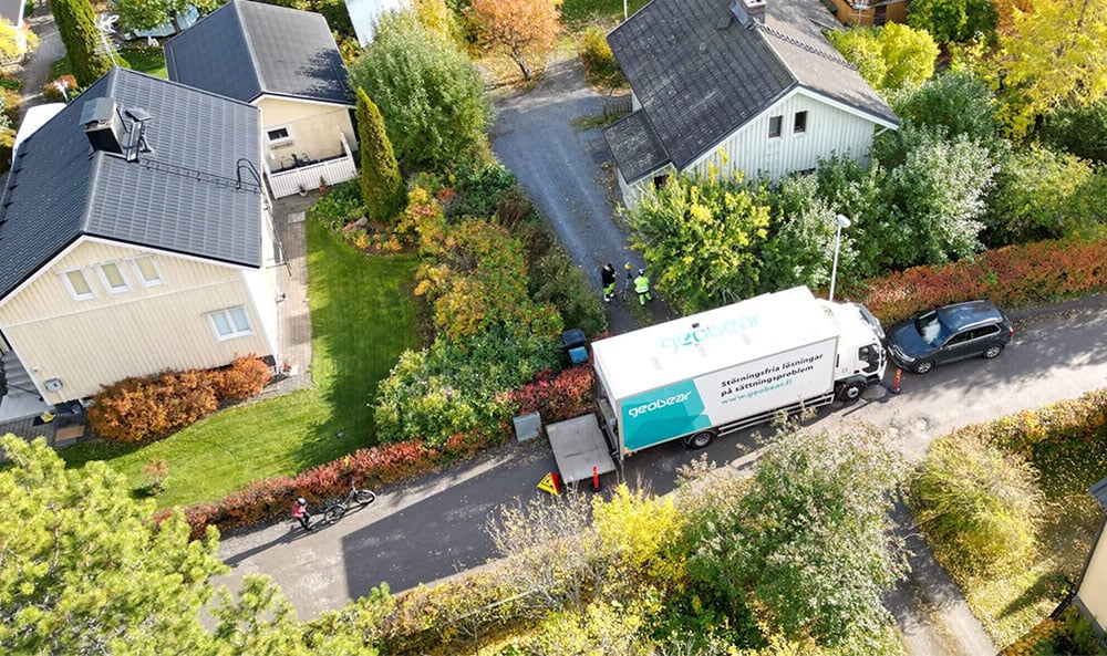 Drönarbild över ett svenskt villaområde i vackert höstväder med Geobears lastbil parkerad.