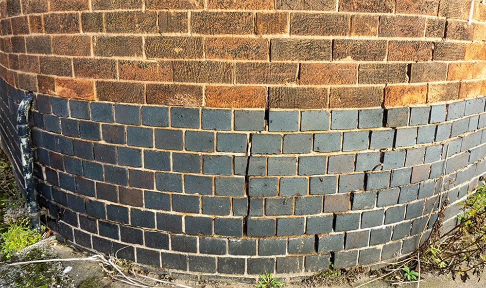 En rundad tegelvägg med sättningsskador/sprickor orsakade av lerkrympning.
