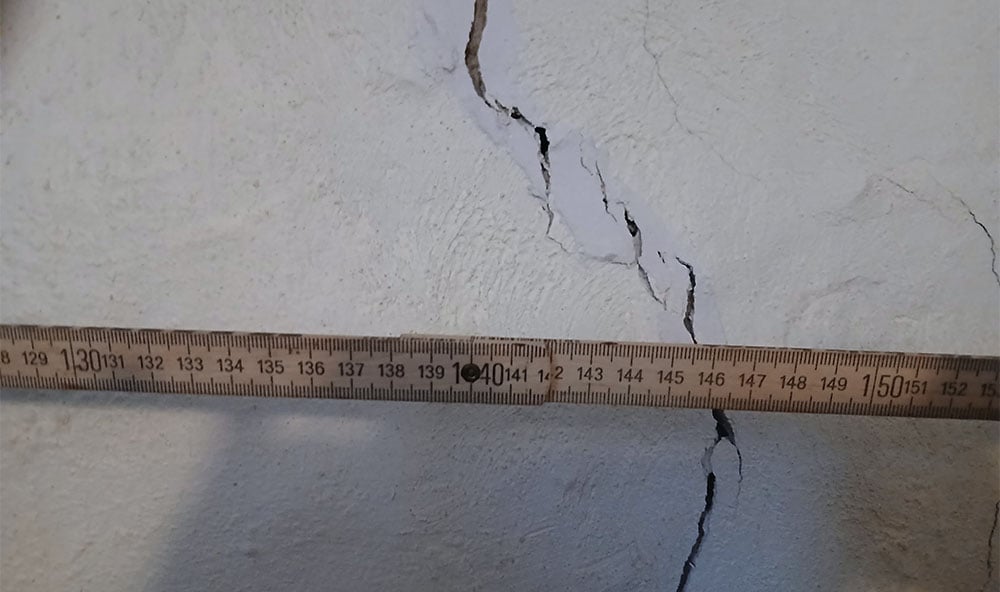 Tegelvilla i Visby med sättningsskador i källargrunden och sprickor i betongplattan. Fastigheten genomgår markförstärkning med Geobears lösning för att stabilisera huset och stoppa framtida sättningar efter uttorkning av marken, en effektiv metod för grundförstärkning utan grävning.