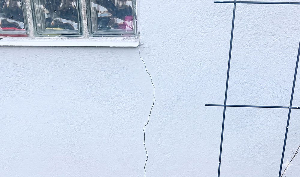 Horisontell spricka i husvägg under fönster orsakat av sättningar.