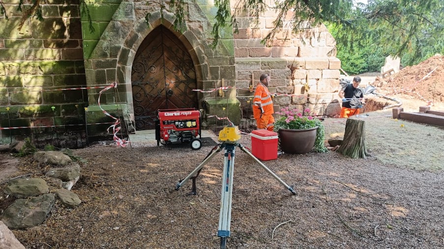A laser level in foreground with Geobear techs at work at the side entrance exterior of St. Mary's Church
