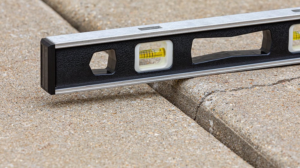 Close-up view of level on top of uneven concrete slab flooring showing a clear gap in slab height.