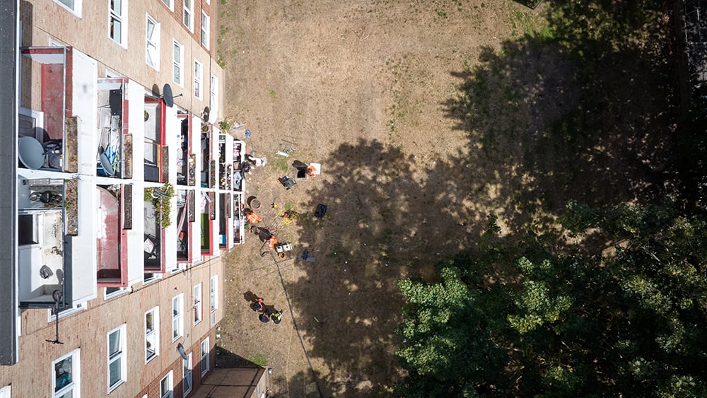Aerial view looking directly down with a block of flats on the left, Geobear tech crew in the block's garden, and trees to the right