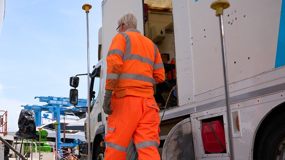 View of Geobear tech walking in front of parked Geobear vehicle, with a large gantry crane in background.