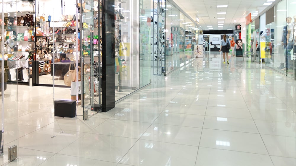 View of white tile floor inside retail space with glass walls of shops on either side of a main hall.