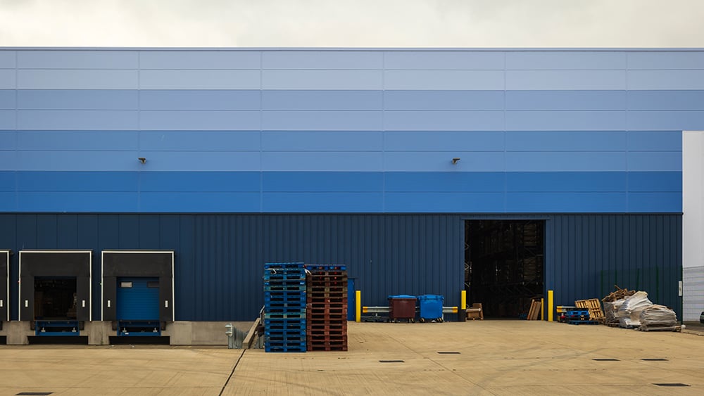 View of receiving doors with stacked pallets and an open bay door at a large building.