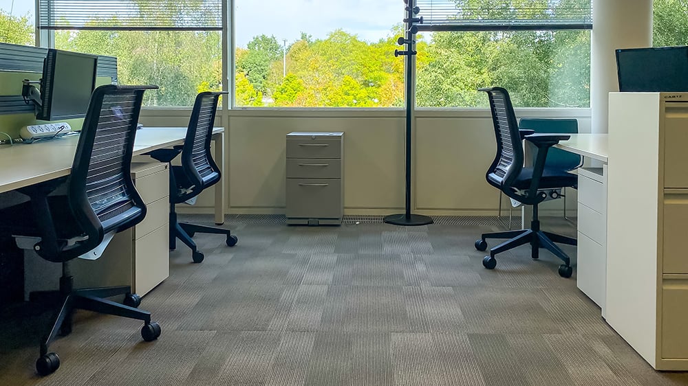 Interior view of office desks with black chairs and a filing cabinet in the background.