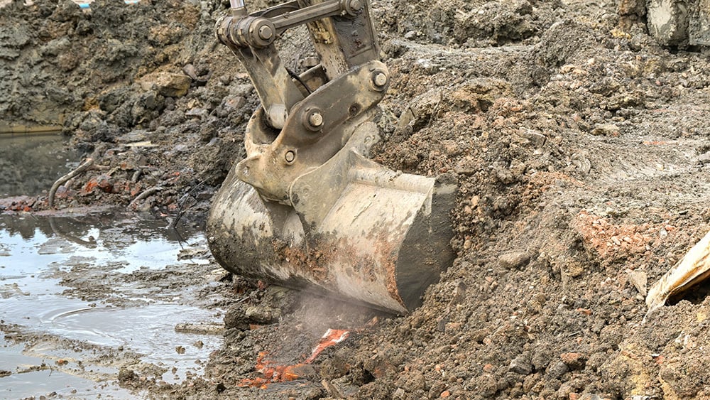 View of a mechanical digger scooping ground in a construction site with a pool of water.