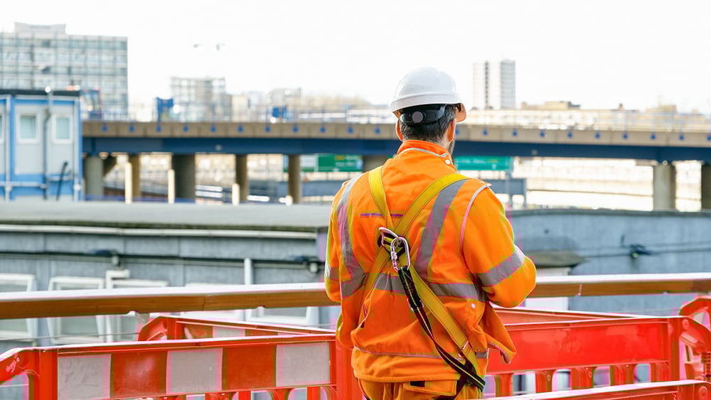 Contractor in orange PPE standing in barricades at a construction site
