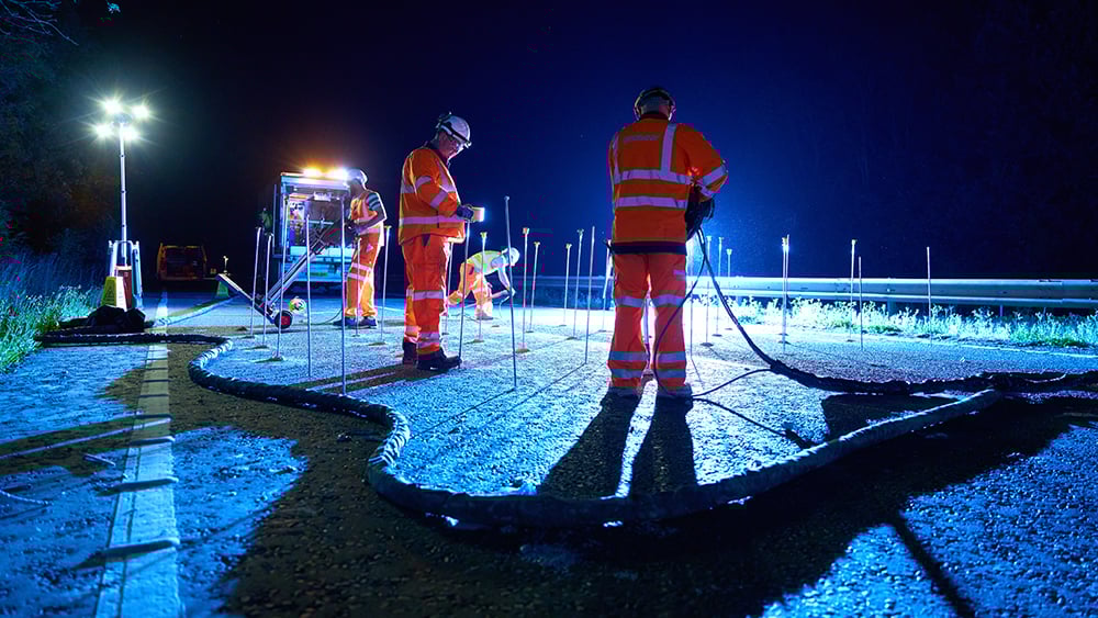 Geobear techs working injection points at night on a motorway with injection system hose in foreground