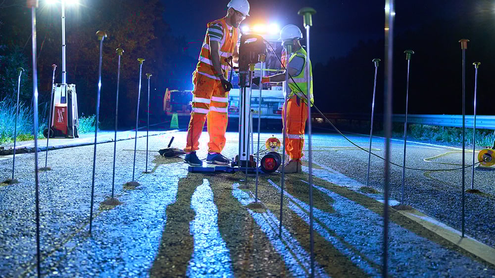 Night shot of drilling rig drilling into motorway surface with injection tube grid in foreground.