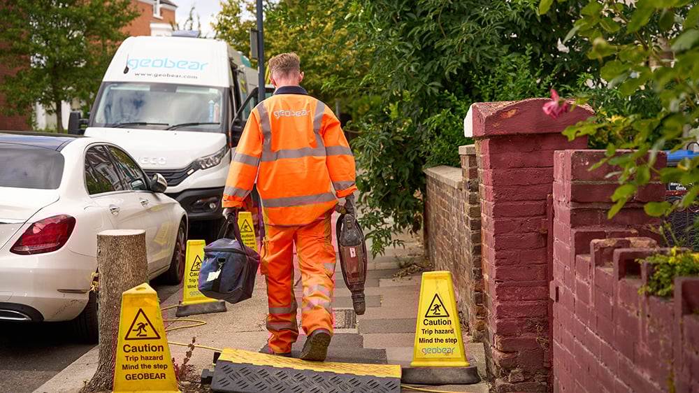 Geobear tech carrying tools walking along city pavement to a Geobear vehicle.