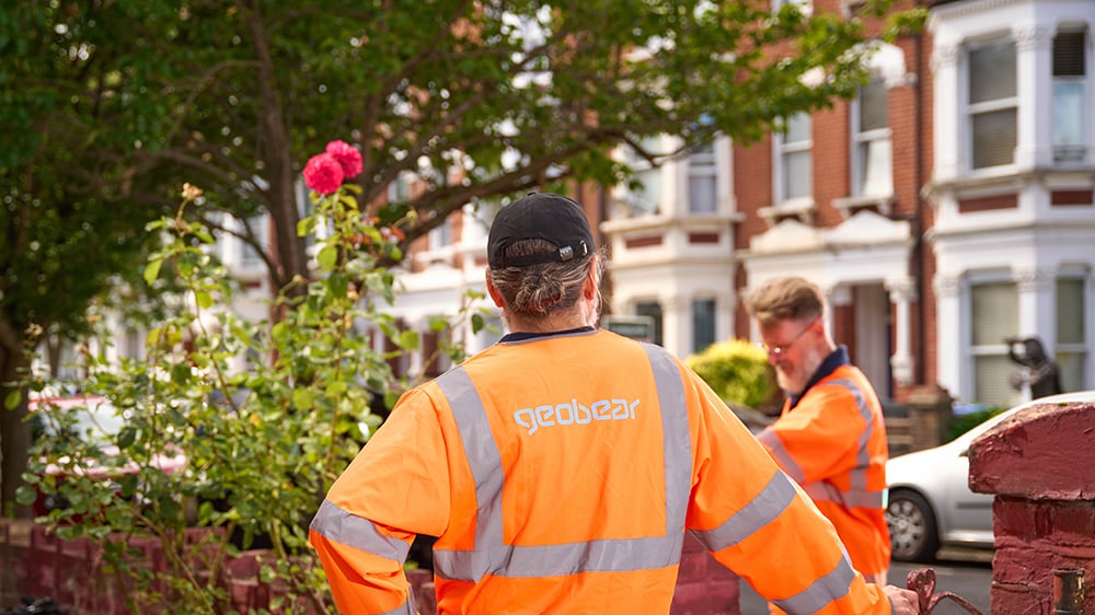 Two Geobear techs preparing job site for residential home with view of terraced homes in background.