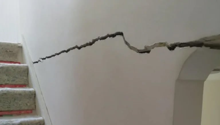 A large horizontal wall crack extends along an internal house wall