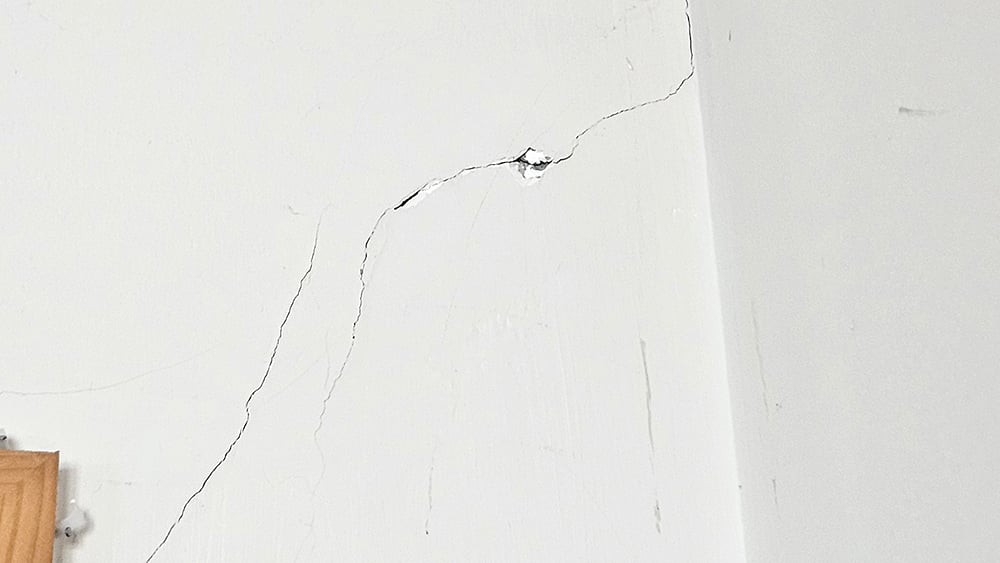 Close up of diagonal cracks moving from top of a door frame to the ceiling on an internal wall of a home.