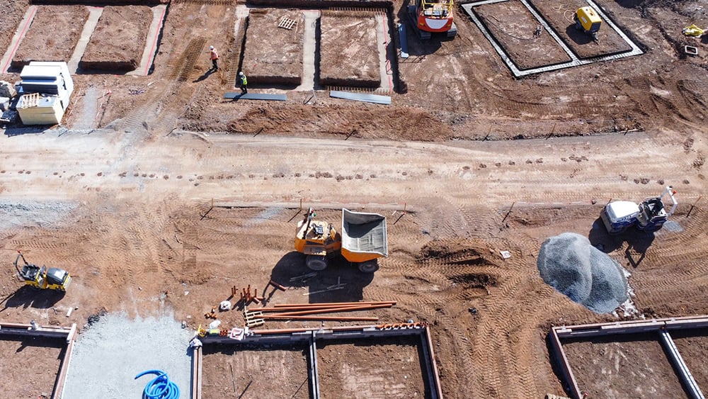 Aerial view of home foundations formed in the soil on an active construction site with building equipment.