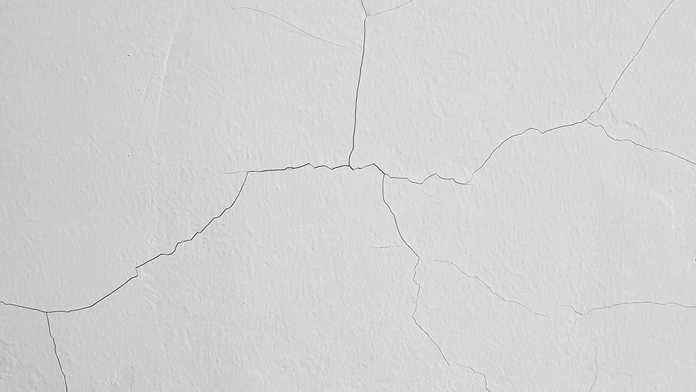 Close up view of series of hairline cracks on a white wall.