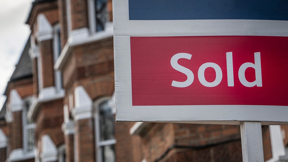 A view of a sold sign in the foreground with a row of residential homes out of focus in the background.