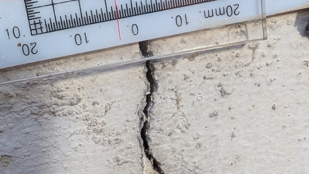 Close up view of exterior home wall crack with crack measuring meter attached.
