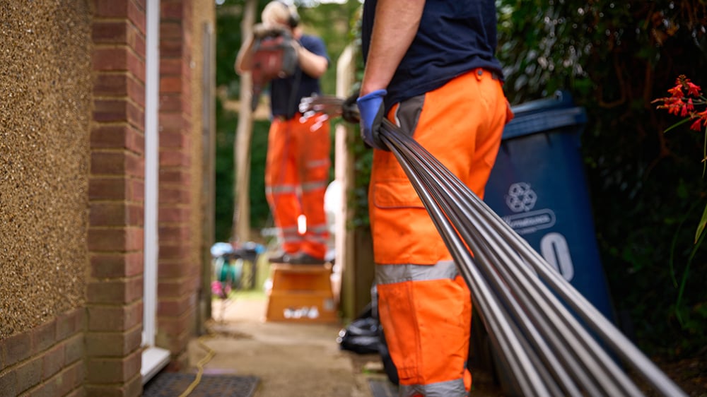 One Geobear tech carries steel injection tubes in the foreground and another drills into a home's foundation.
