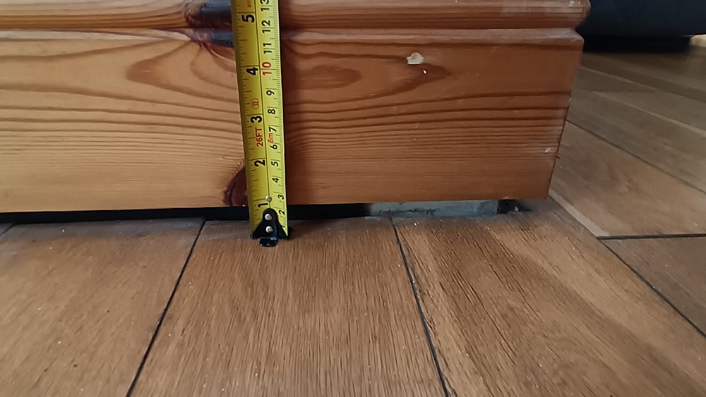 View of sunken floor gap to baseboard with measuring tape to show floor drop