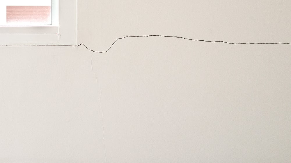 Close up of a horizontal crack originating from the bottom right corner of a window along the internal wall of a home.